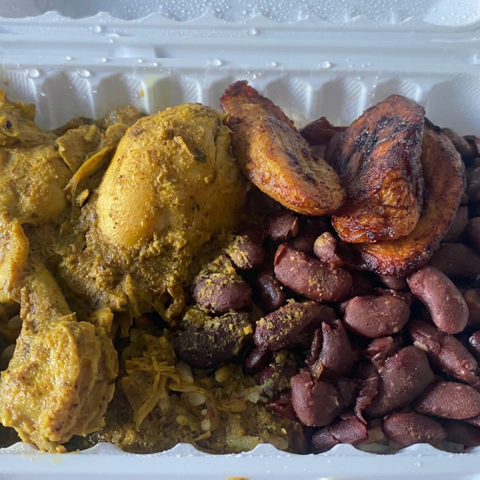 Open takeout container filled with curry chicken, rice, red beans, and fried plantains.