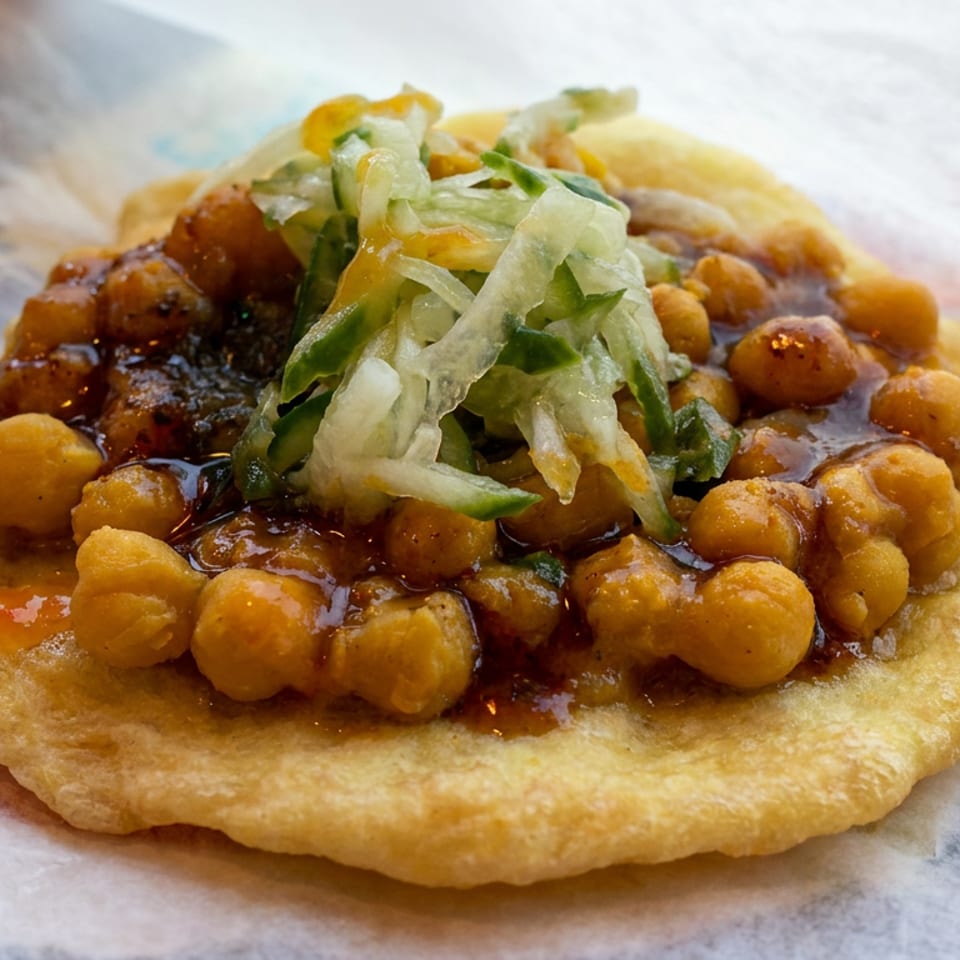 Crispy fried flatbread topped with chickpeas, dark sauce, shredded lettuce, and chopped vegetables.