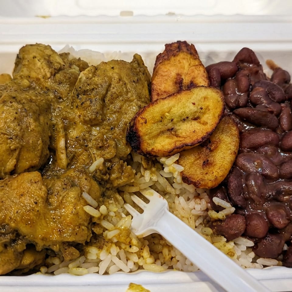 Takeout container filled with rice, stewed meat, red beans, and fried plantains, with a white plastic fork.